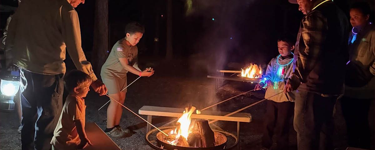 Families roasting marshmallows around a campfire during a relaxing camping weekend at Jellystone Park™ Asheboro