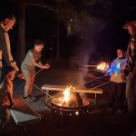 Families roasting marshmallows around a campfire during a relaxing camping weekend at Jellystone Park™ Asheboro
