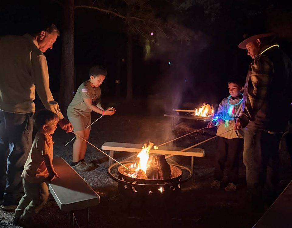 Families roasting marshmallows around a campfire during a relaxing camping weekend at Jellystone Park™ Asheboro