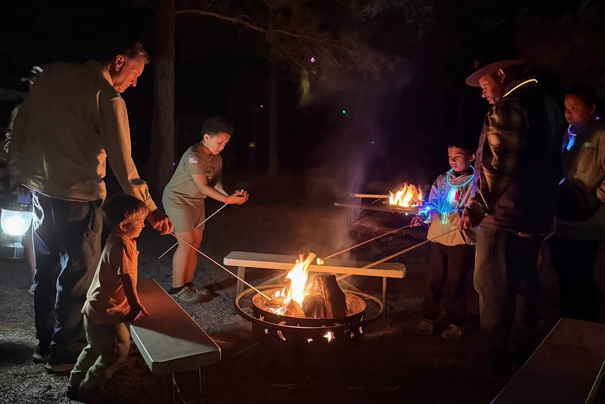 Families roasting marshmallows around a campfire during a relaxing camping weekend at Jellystone Park™ Asheboro