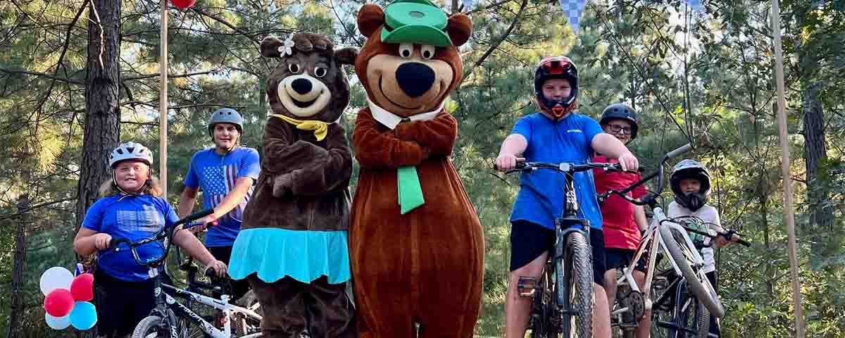 Family enjoying bikes and activities with Yogi Bear and Cindy Bear at Asheboro Jellystone Park in North Carolina