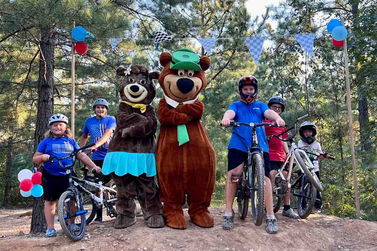 Family enjoying bikes and activities with Yogi Bear and Cindy Bear at Asheboro Jellystone Park in North Carolina