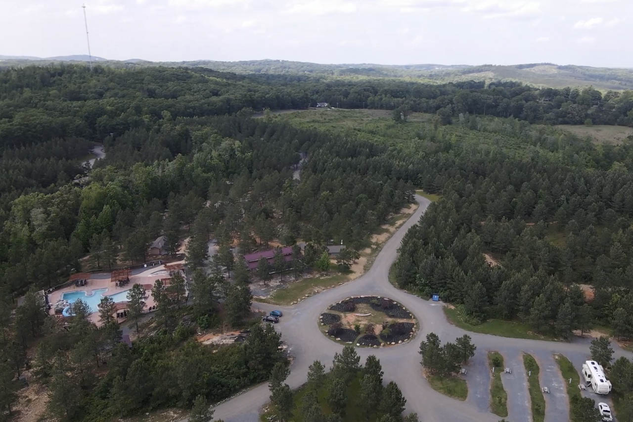Aerial view of Jellystone Park Asheboro showing wooded campground grounds, paved roads, swimming pool and RV campsites