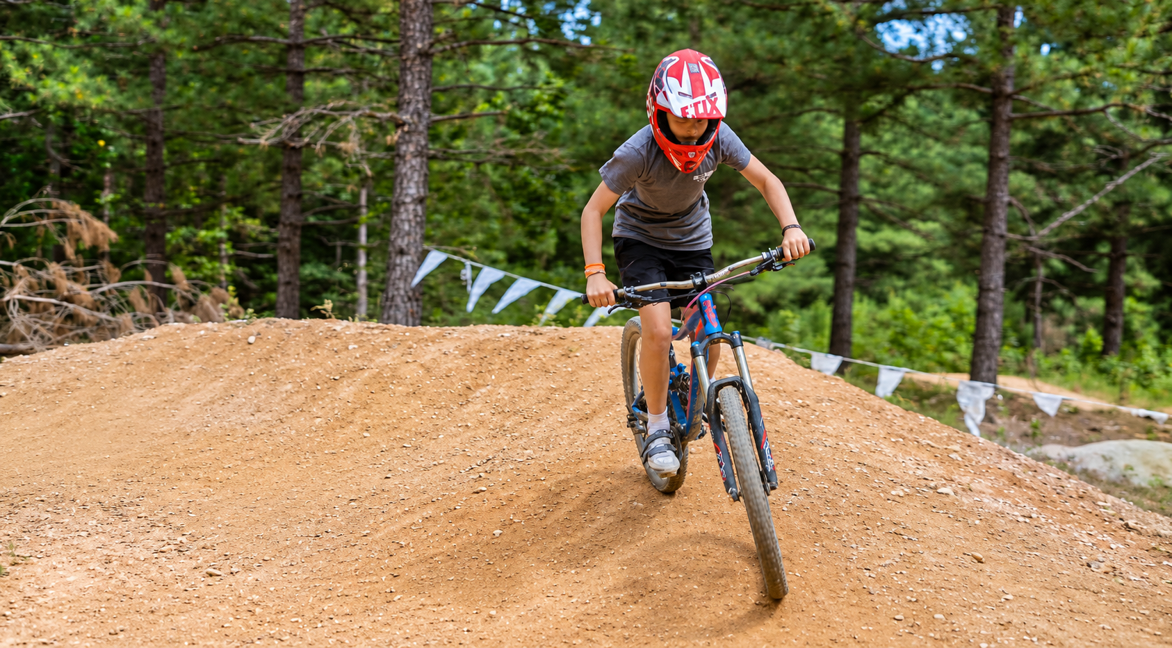 Young cyclist wearing a helmet riding a mountain bike on the dirt pump track at Jellystone Park Asheboro